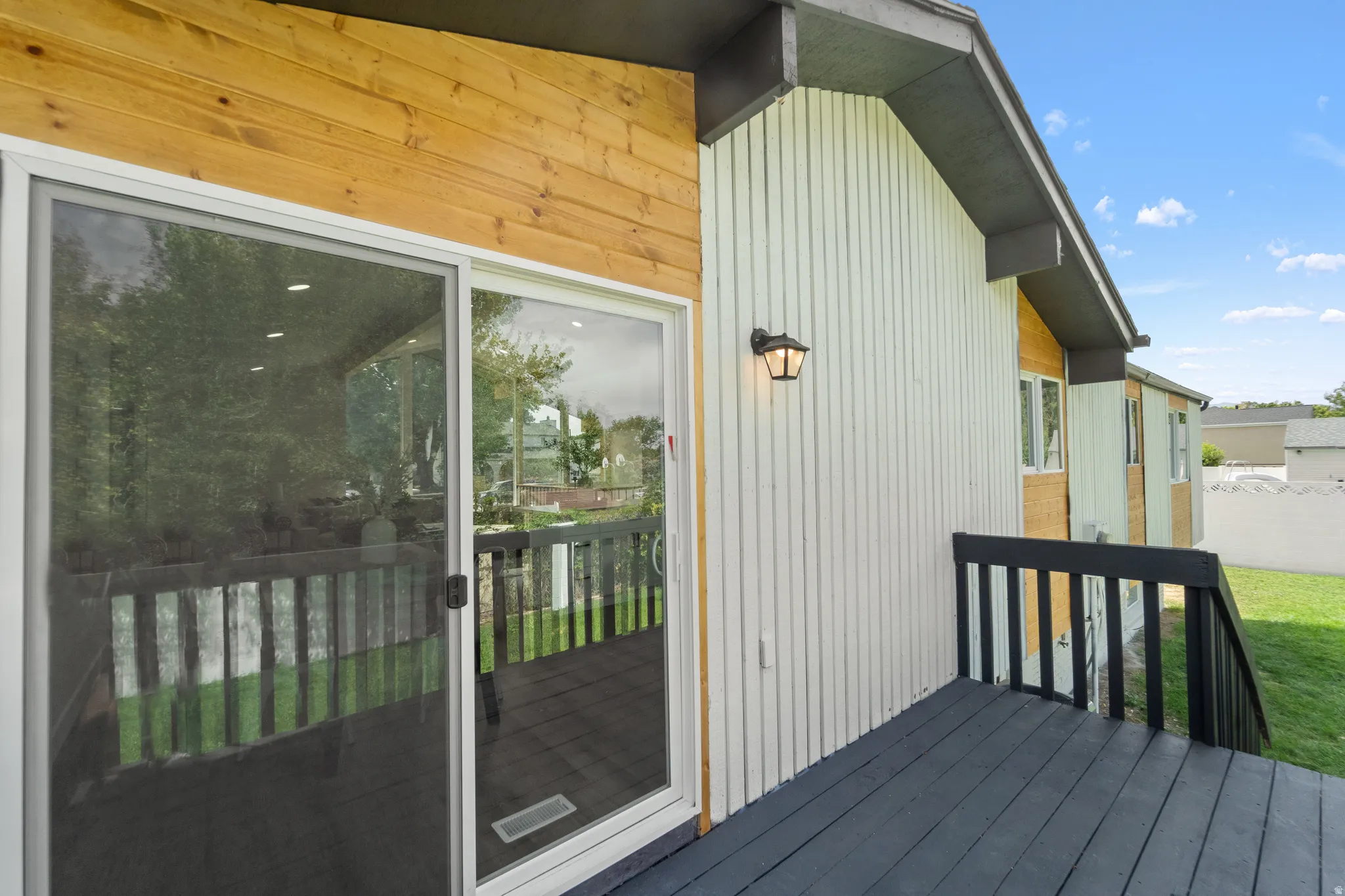 Deck with black railings, sliding glass doors, horizontal wood siding, vertical panel siding, and exterior wall lantern