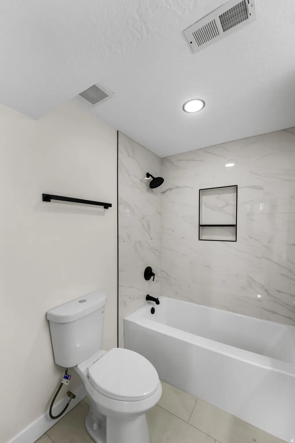 White bathtub with matte black fixtures, marble-patterned tile surround, and recessed shower niche