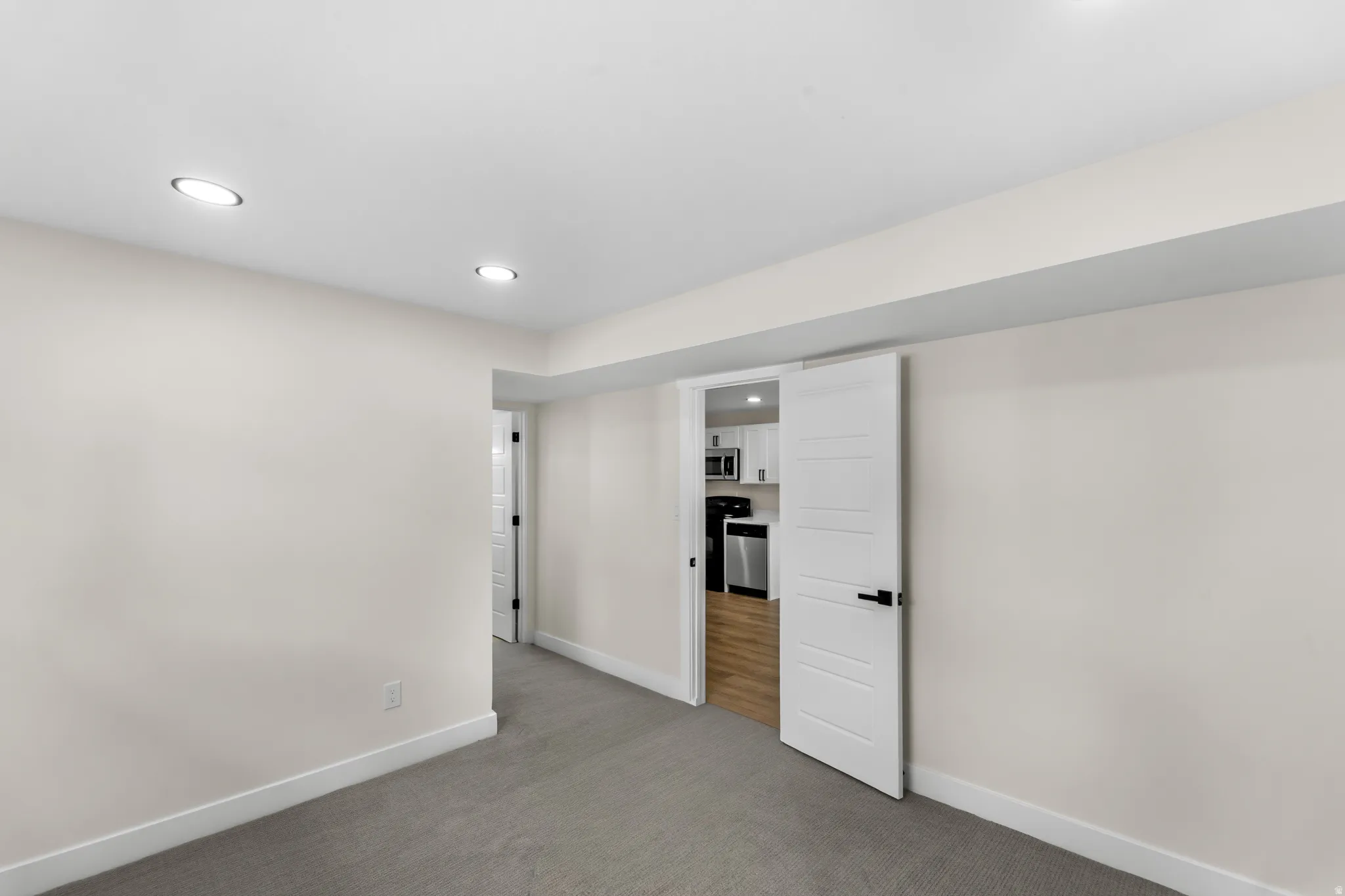 Recessed lighting, light gray carpeting, neutral wall paint, modern white doors, and wood-finish flooring visible in the distance
