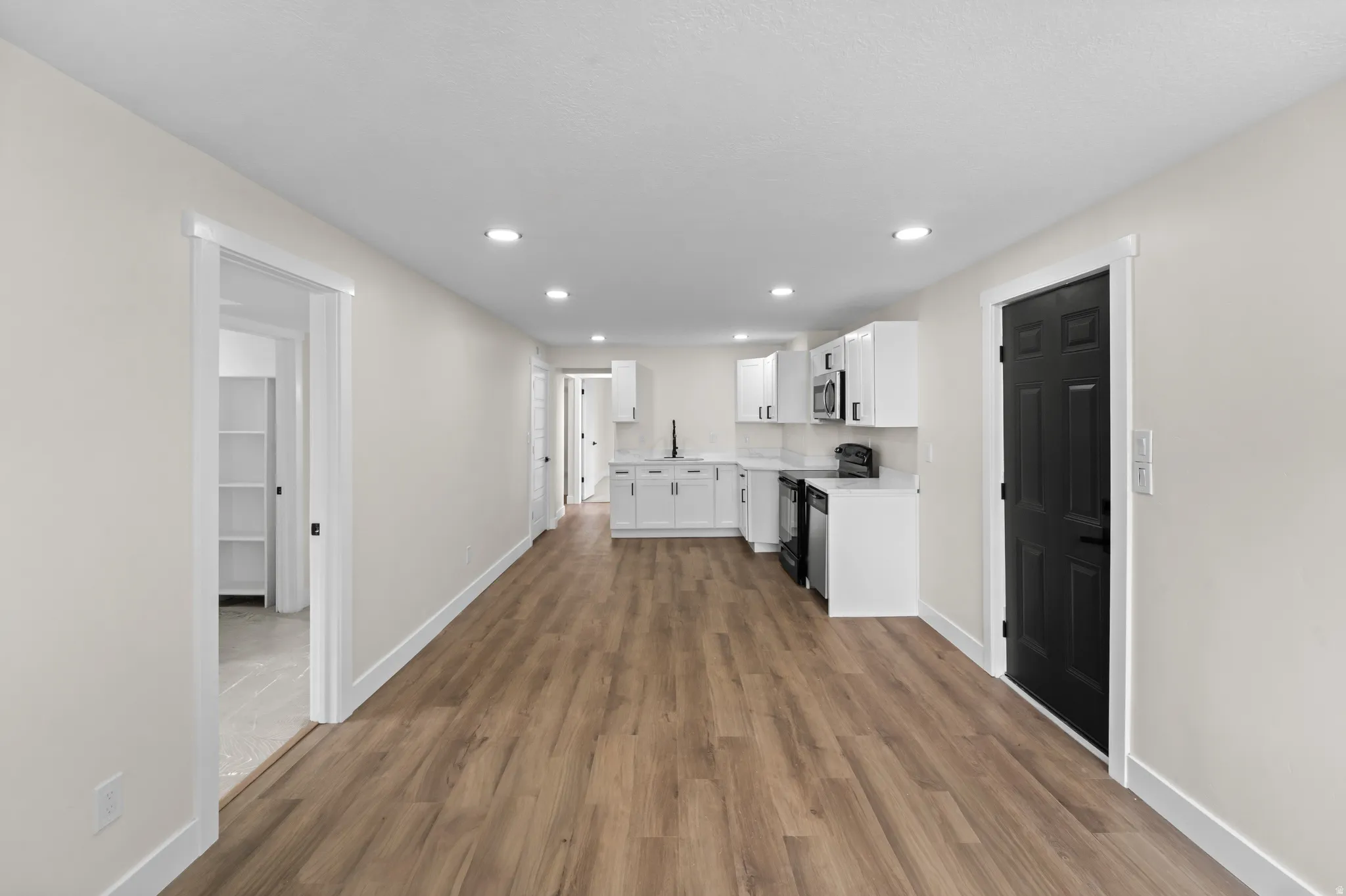 Open-concept layout with wood-finish flooring, recessed lighting, and a kitchen featuring white cabinetry, light countertops, and stainless steel appliances