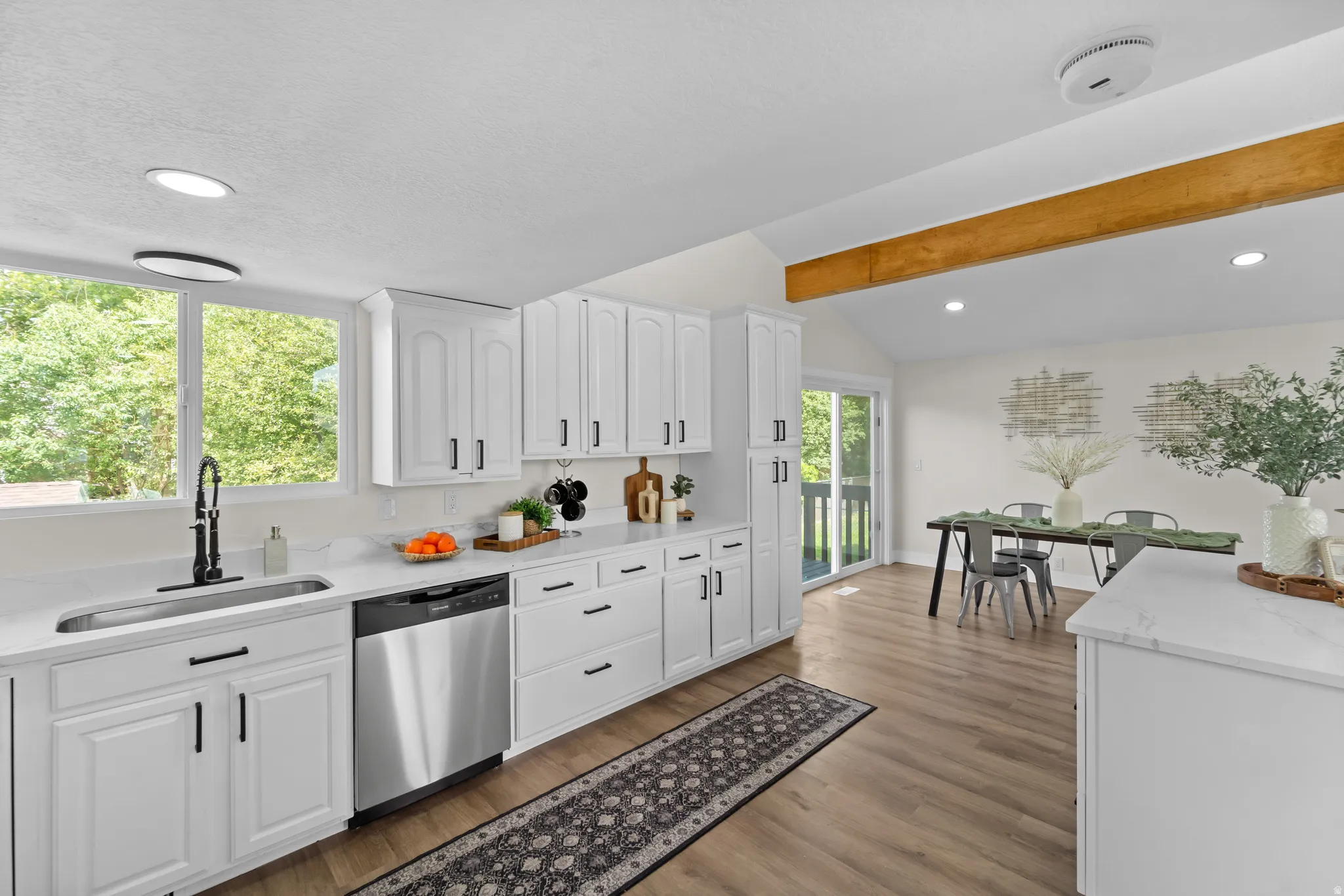 Kitchen with white cabinetry, stainless steel dishwasher, and wood-finish flooring