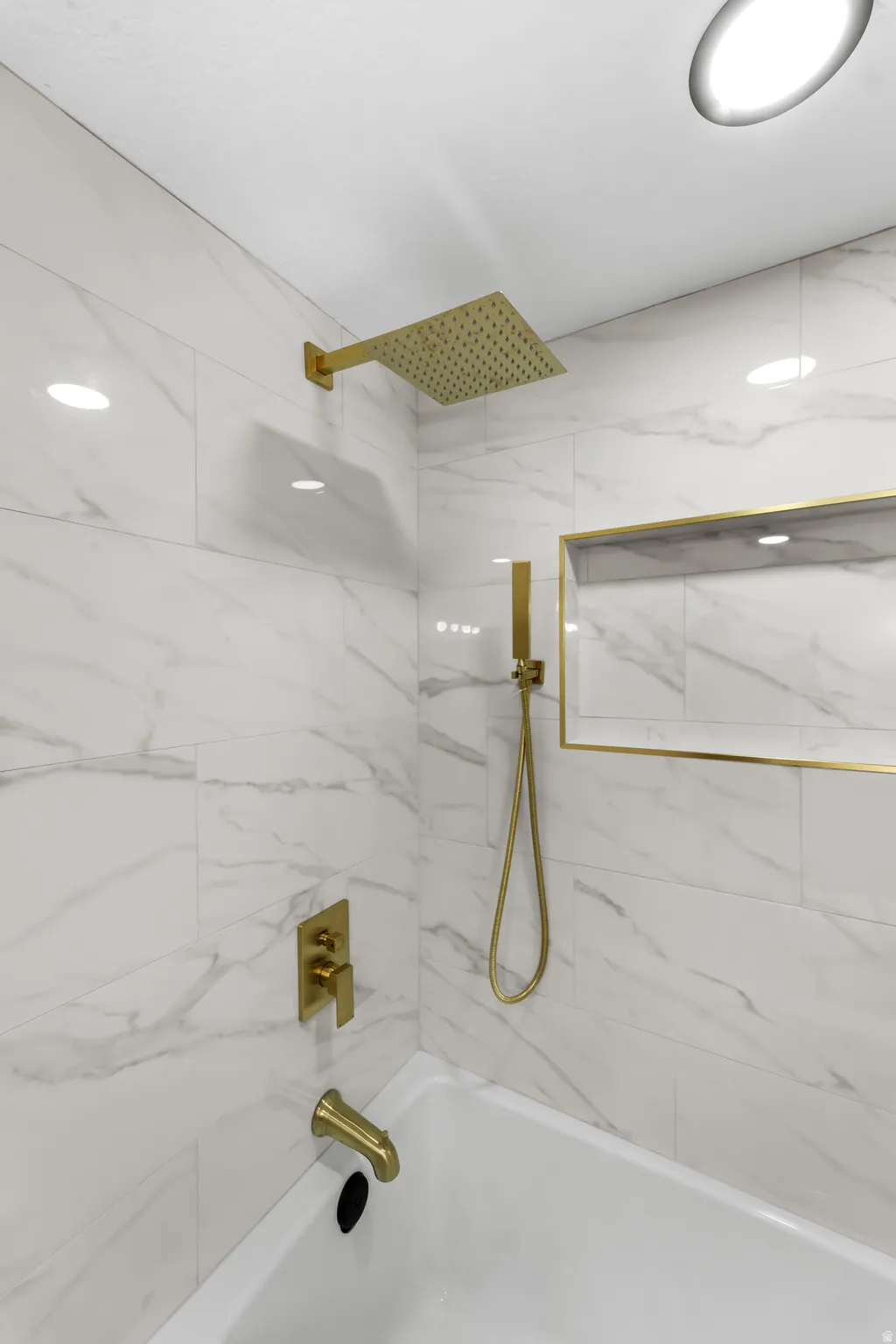 Bathtub featuring a rainfall showerhead, handheld shower, and tub filler, all in a gold finish