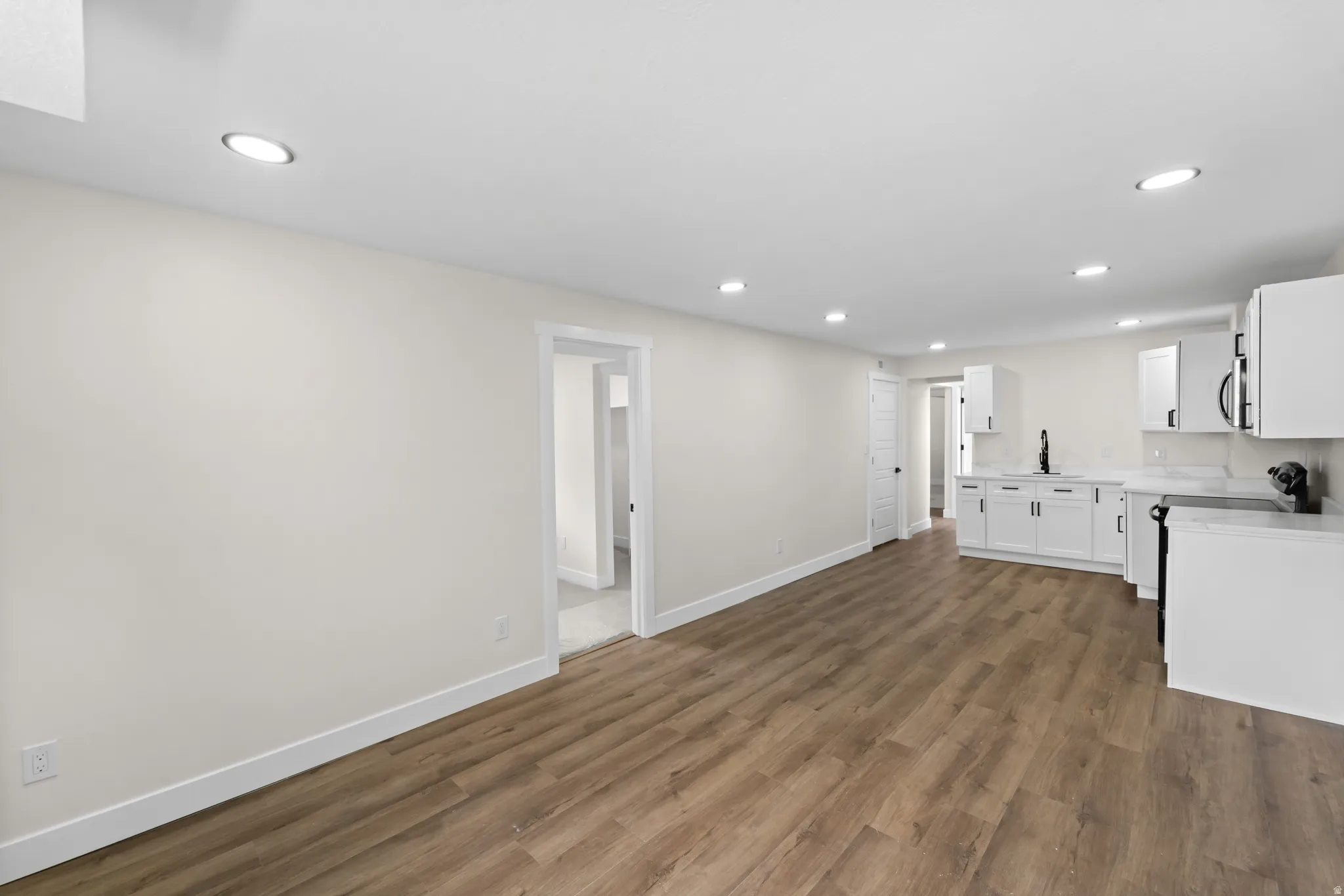 Open-concept living space featuring wood-finish flooring, recessed lighting, and a kitchen with white cabinetry and countertops