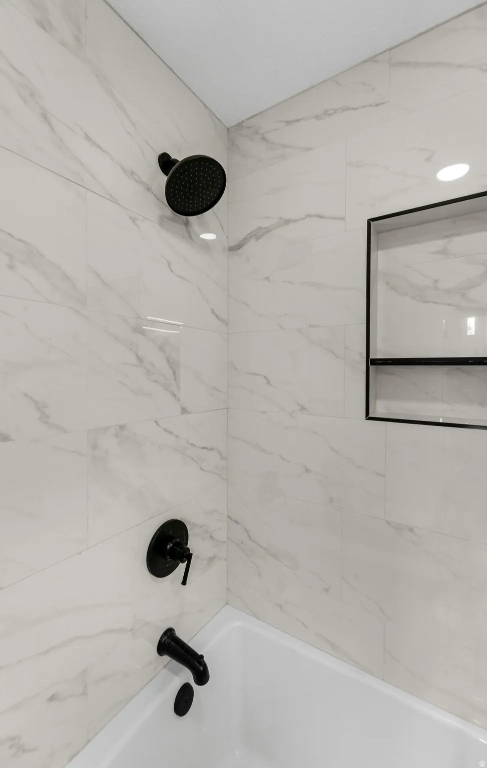Bathtub with matte black fixtures, white tile surround, recessed lighting, and a built-in shower niche
