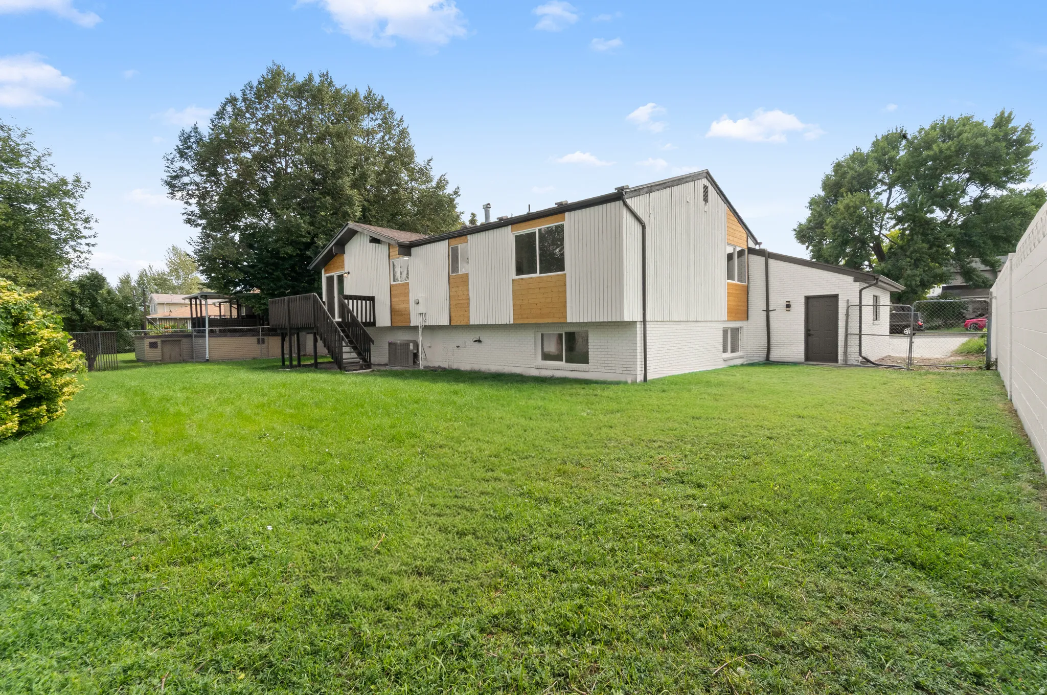 Expansive grassy yard with mature trees, a multi-level deck, and a detached building