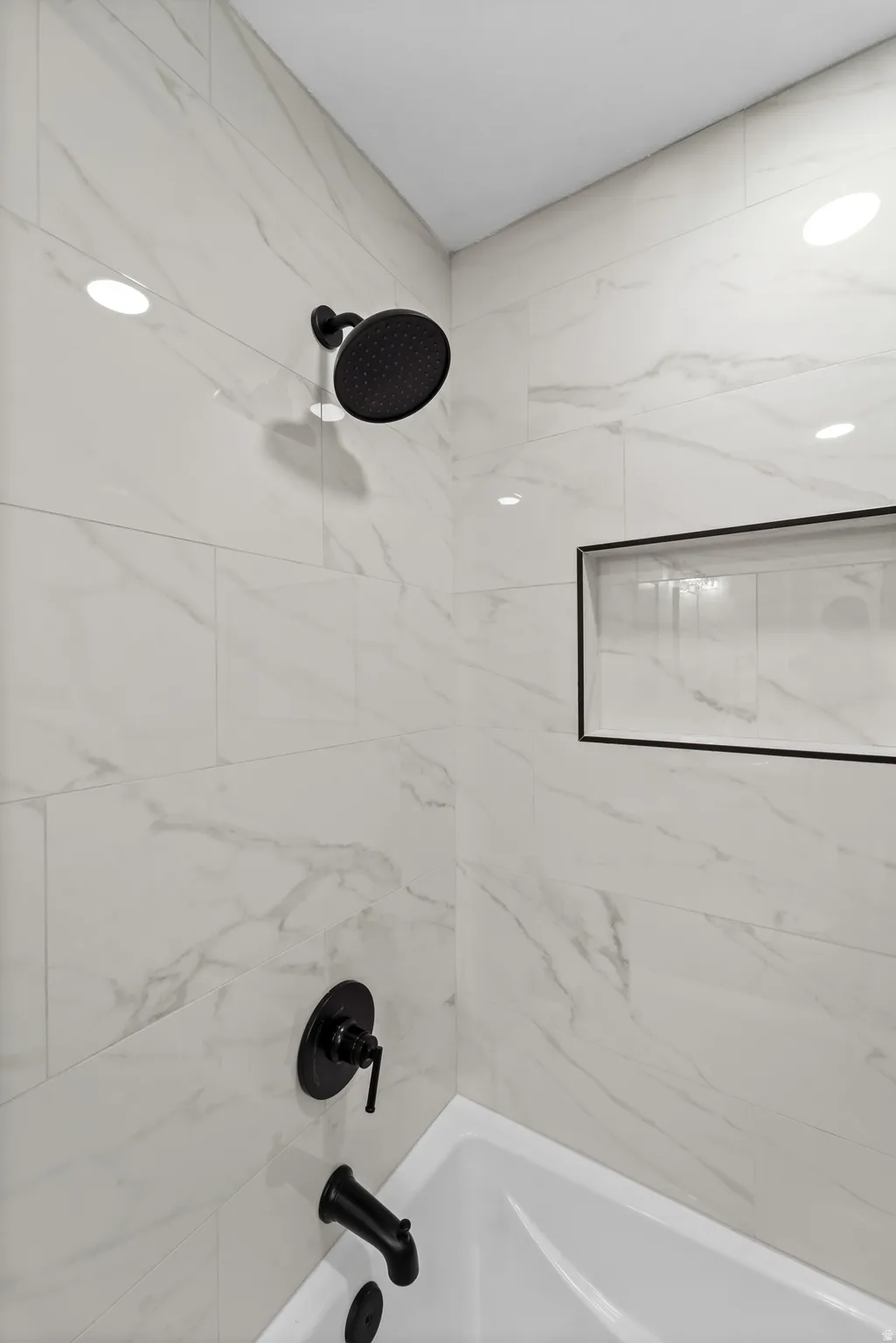 White tiled shower surround with dark contrasting fixtures