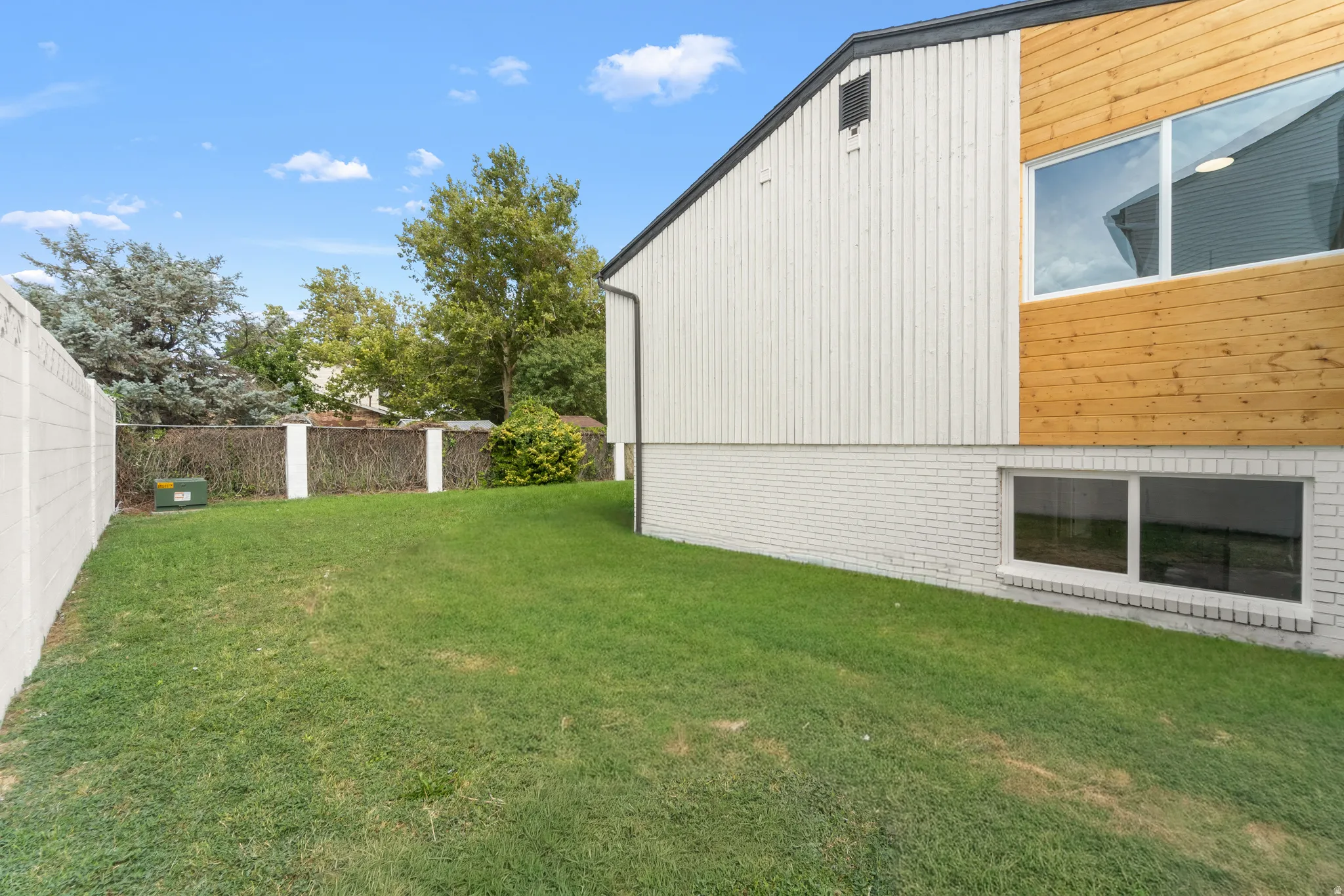 Expansive green space featuring a concrete block fence, brick foundation, and horizontal wood siding accents
