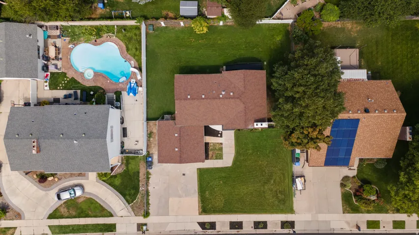 Asphalt shingle roofing, solar panel array, concrete driveway, front lawn, and established landscaping