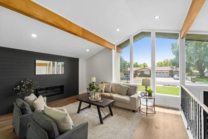 Vaulted ceiling with exposed wood beams, expansive window array, wood-finish flooring, recessed lighting, and a built-in linear fireplace