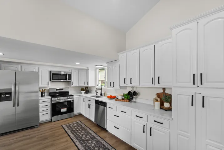 White cabinetry with black hardware, stainless steel appliances, wood-finish flooring, white countertops, and vaulted ceilings