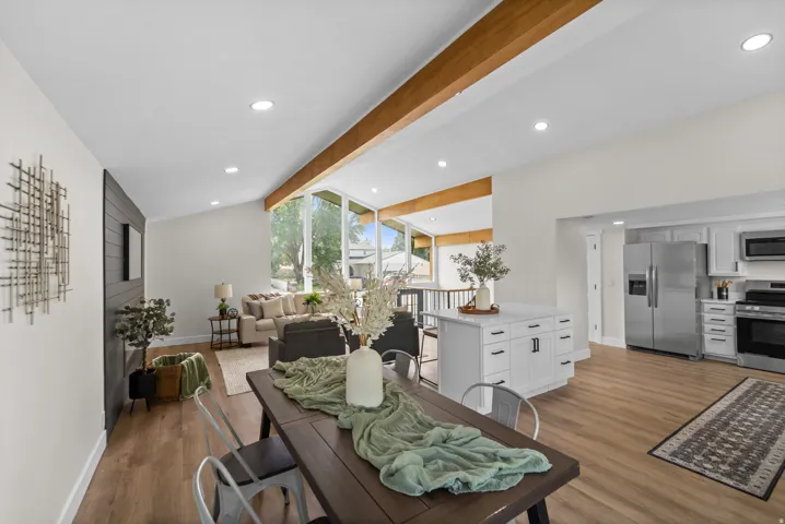 Vaulted ceilings with exposed wood beams, recessed lighting, wood-finish flooring, and a kitchen featuring stainless steel appliances