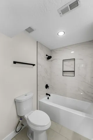 White bathtub with matte black fixtures, marble-patterned tile surround, and recessed shower niche