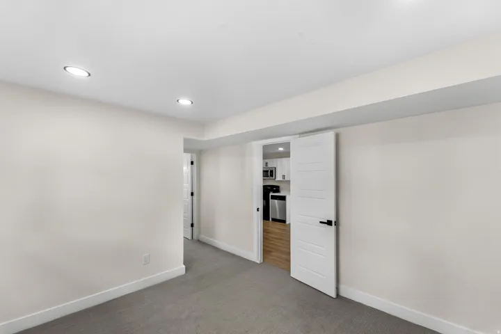 Recessed lighting, light gray carpeting, neutral wall paint, modern white doors, and wood-finish flooring visible in the distance