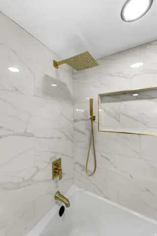Bathtub featuring a rainfall showerhead, handheld shower, and tub filler, all in a gold finish