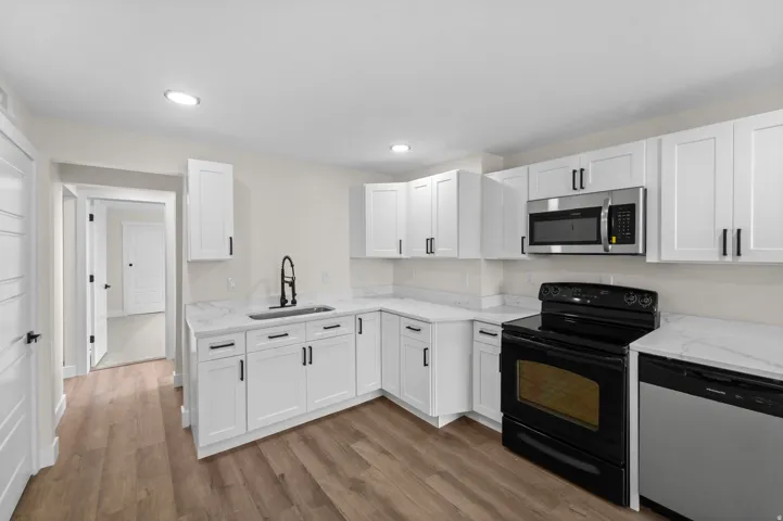 Kitchen featuring white shaker cabinetry, light-toned countertops, a stainless steel microwave, a black electric range, and wood-finish flooring