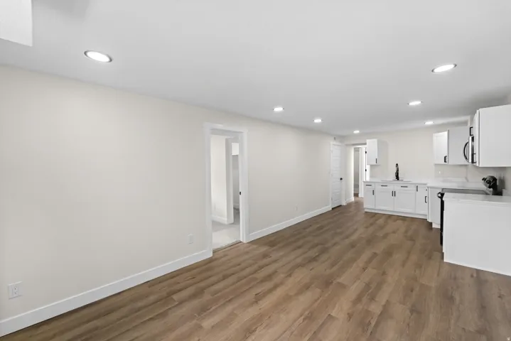 Open-concept living space featuring wood-finish flooring, recessed lighting, and a kitchen with white cabinetry and countertops