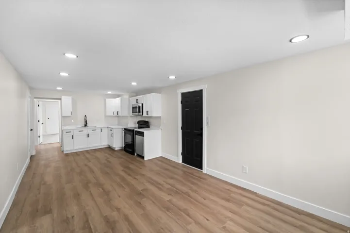 Open-concept layout with wood-finish flooring, recessed lighting, and a kitchen featuring white cabinetry, light-colored countertops, and stainless steel appliances