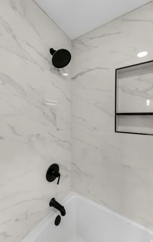 Bathtub with matte black fixtures, white tile surround, recessed lighting, and a built-in shower niche
