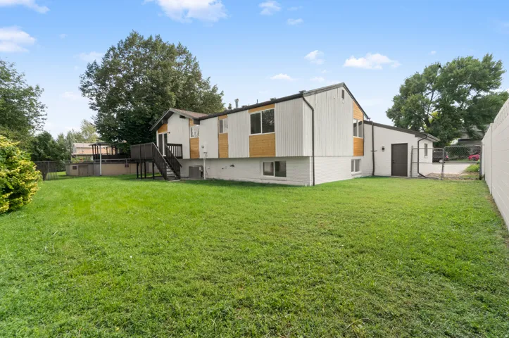 Expansive grassy yard with mature trees, a multi-level deck, and a detached building
