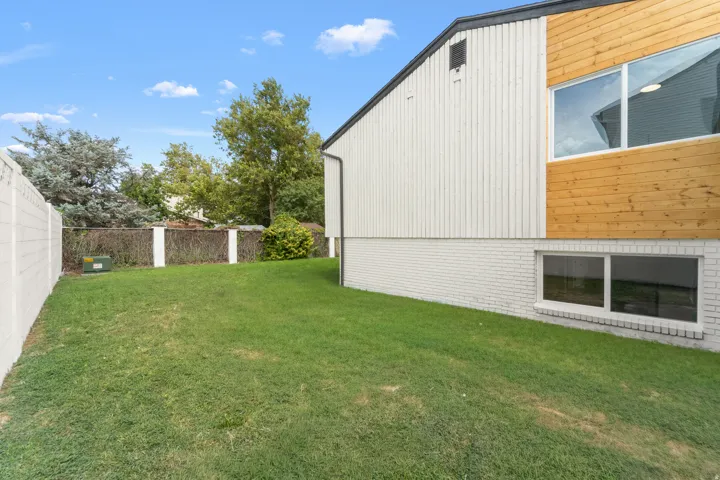 Expansive green space featuring a concrete block fence, brick foundation, and horizontal wood siding accents