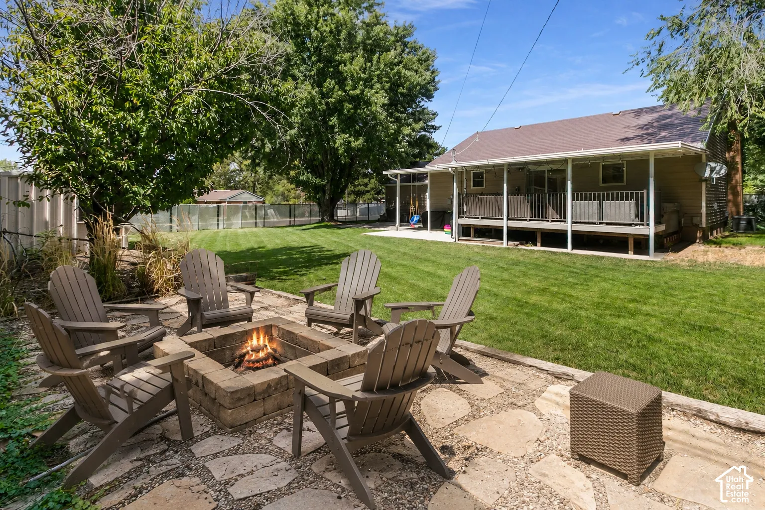 Expansive lawn with a stone-paved patio, a built-in stone fire pit, and mature trees