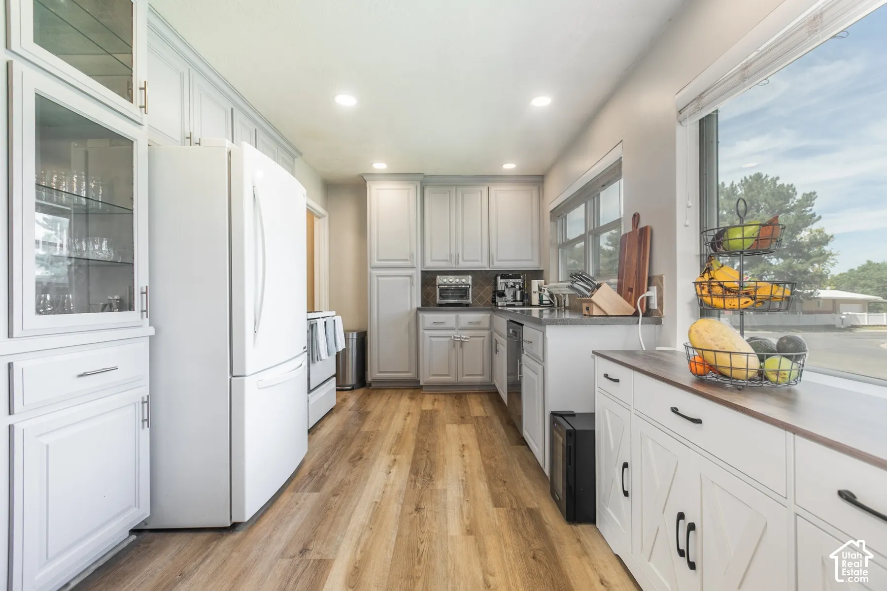 Recessed lighting, wood-finish flooring, white cabinetry with display glass, large windows, and dark countertops