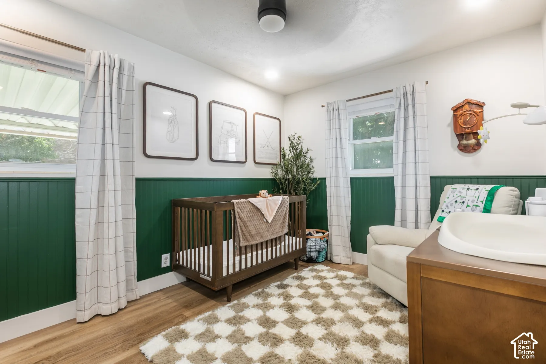 Recessed ceiling lighting, wood-finish flooring, two large windows, white walls, and green wainscoting