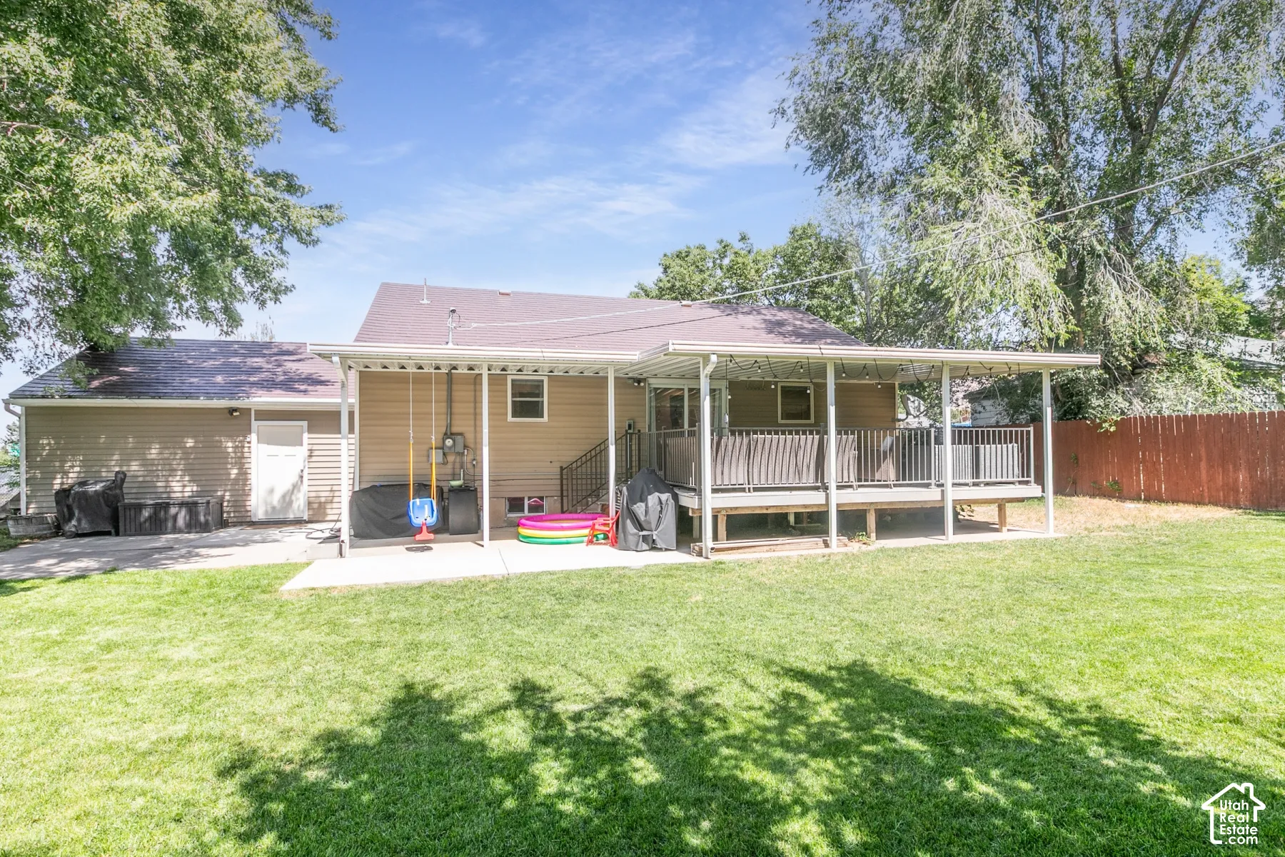 Expansive backyard featuring a covered patio, raised deck, and concrete slab