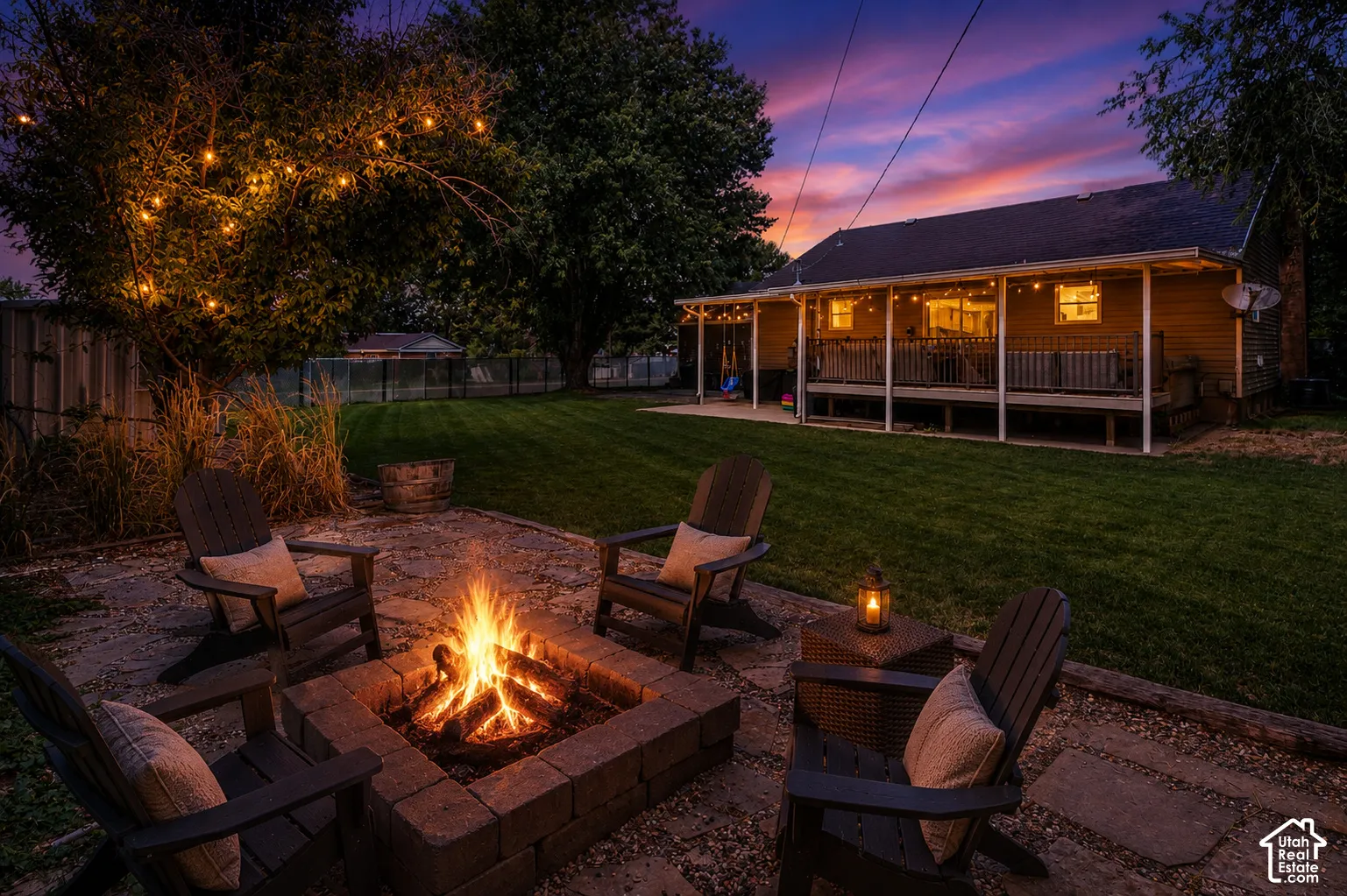 Expansive backyard featuring a manicured lawn, a stone paver patio, a built-in stone fire pit, and a covered back porch with string lighting