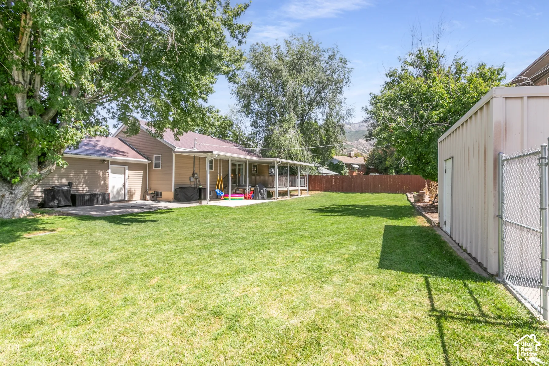 Expansive lawn area, covered patio, privacy fencing, detached utility building, and mature perimeter trees