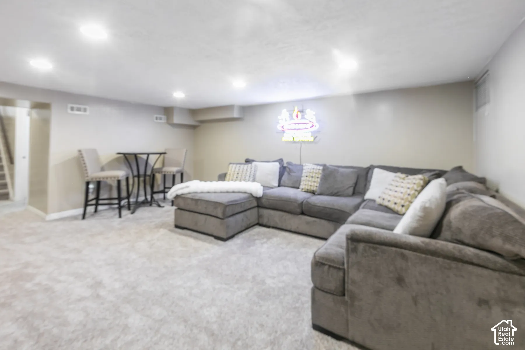 Recessed lighting illuminates this carpeted space featuring light gray walls and a visible staircase