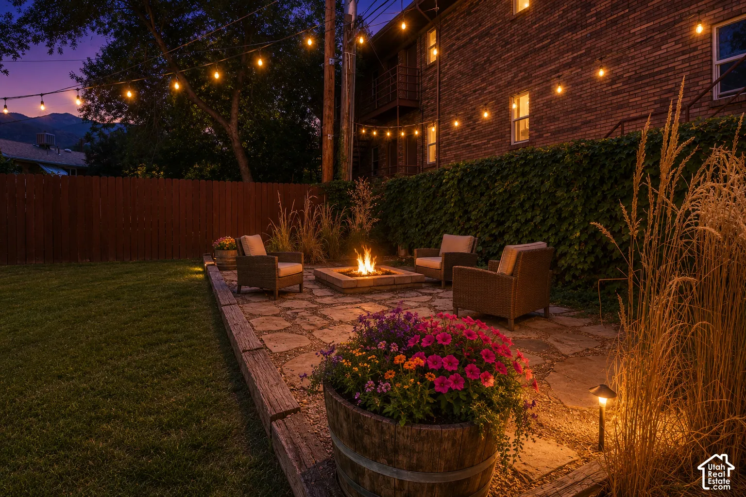Expansive lawn area with a stone patio, built-in fire pit, and string lighting