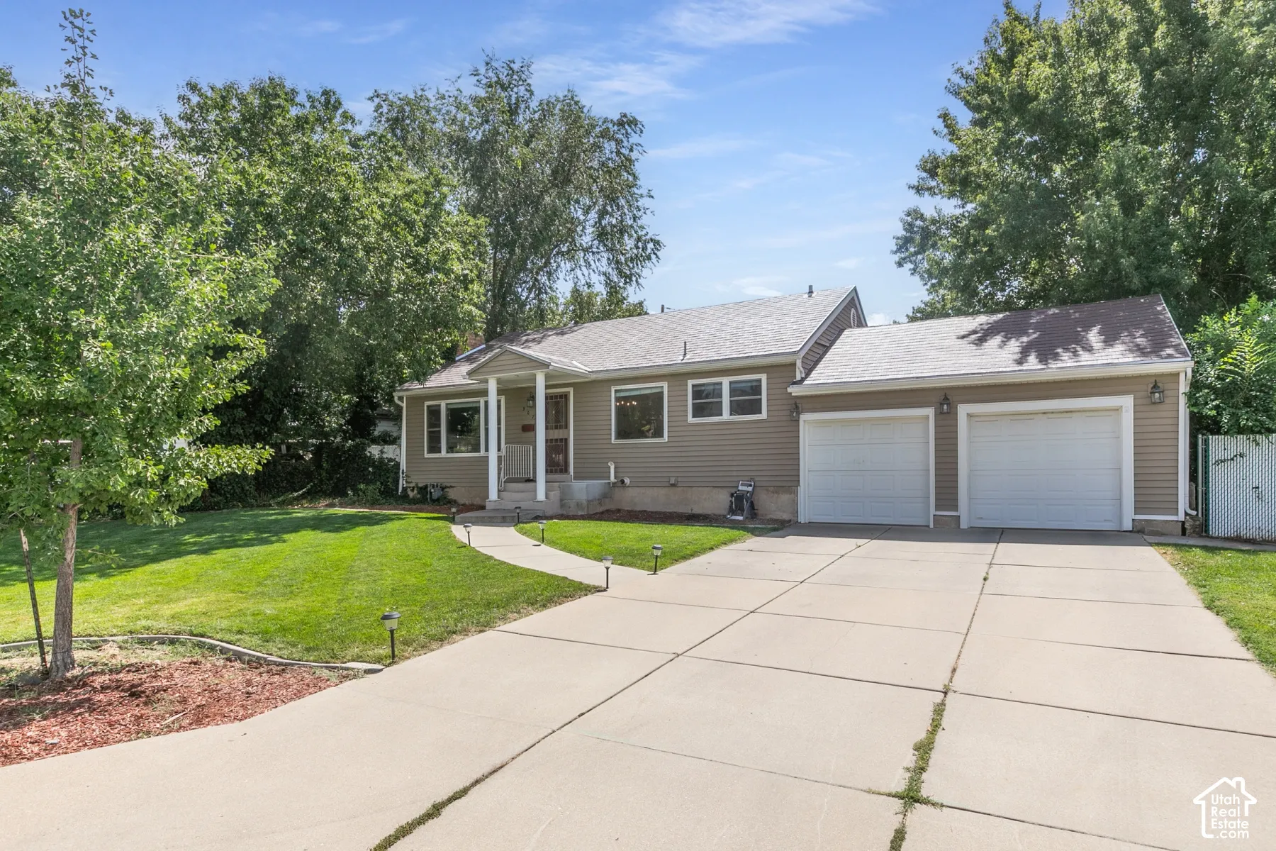 Welcoming ranch-style home featuring a taupe exterior, dual-car garage with white overhead doors, and a concrete driveway