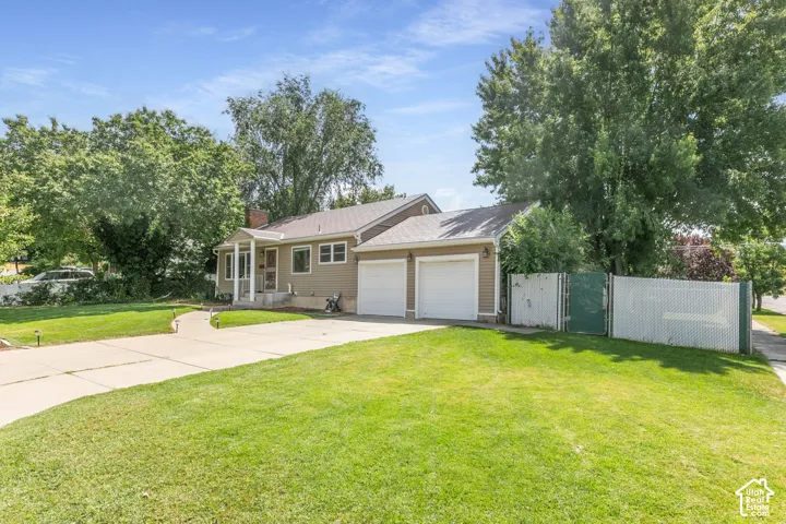 Two-car garage with white doors, light brown siding exterior, covered front porch, concrete driveway, and established green landscaping