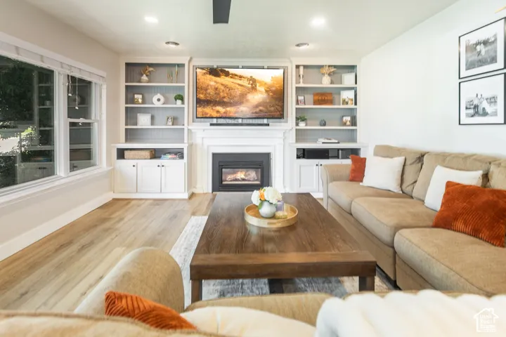Built-in shelving flanking a fireplace with a classic mantel, wood-finish flooring, recessed lighting, and a large window