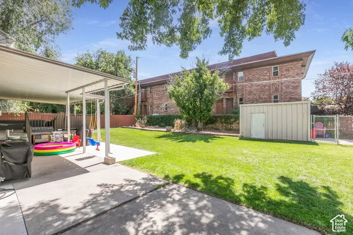 Expansive lawn with a covered patio, concrete paving, and a detached storage shed