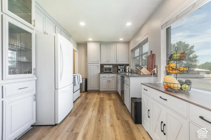 Recessed lighting, wood-finish flooring, white cabinetry with display glass, large windows, and dark countertops