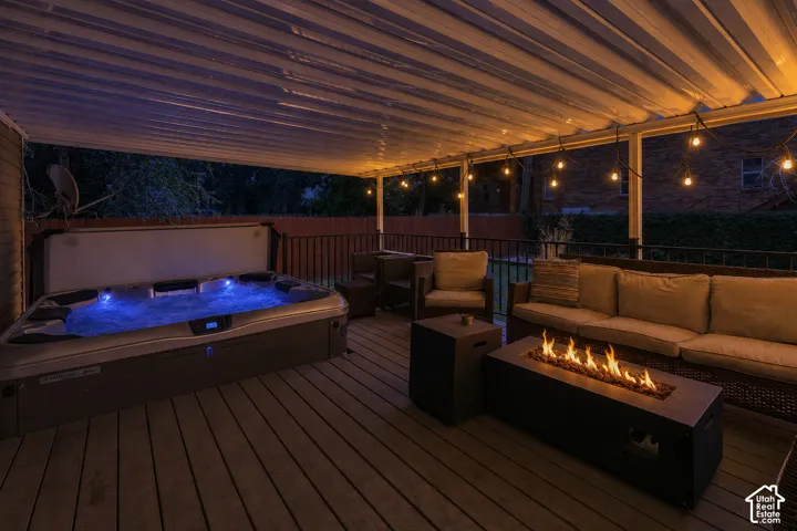 Covered outdoor deck featuring a built-in hot tub, string lighting, and a fire pit