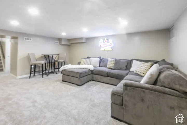 Recessed lighting illuminates this carpeted space featuring light gray walls and a visible staircase
