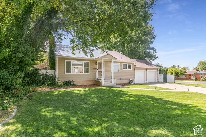 Manicured front lawn with mature trees, a two-car garage, and a light-colored siding exterior