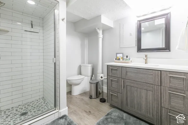 Walk-in shower with subway tile surround and mosaic floor, single vanity with integrated sink and chrome-finish faucet, wood-finish cabinetry, and framed mirror