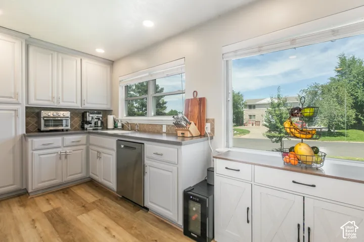 White cabinetry, stainless steel dishwasher, wood-finish flooring, and a window overlooking exterior landscaping