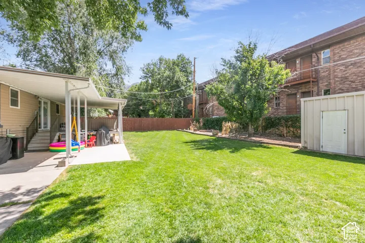 Expansive lawn area with a covered patio, adjacent storage shed, and surrounding privacy fencing