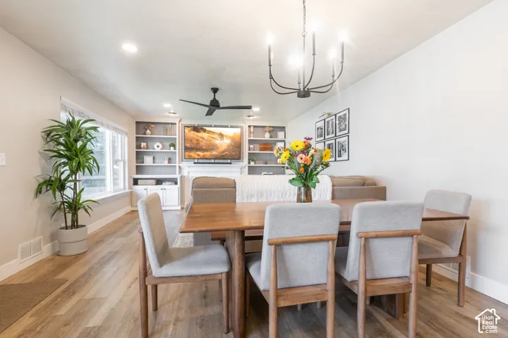 Wood-finish flooring, recessed lighting, and a black chandelier illuminate the living and dining areas
