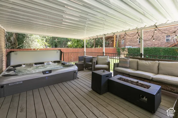 Expansive covered deck featuring a bubbling hot tub, durable wood-finish flooring, and a built-in fire pit