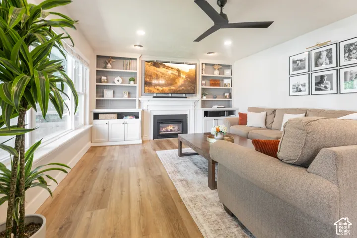 Wood-finish flooring throughout, complemented by a white fireplace and built-in shelving, recessed lighting, and a dark-toned ceiling fan