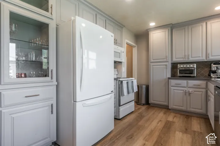 White paneled refrigerator, built-in microwave, wood-finish flooring, recessed lighting, and grey cabinetry