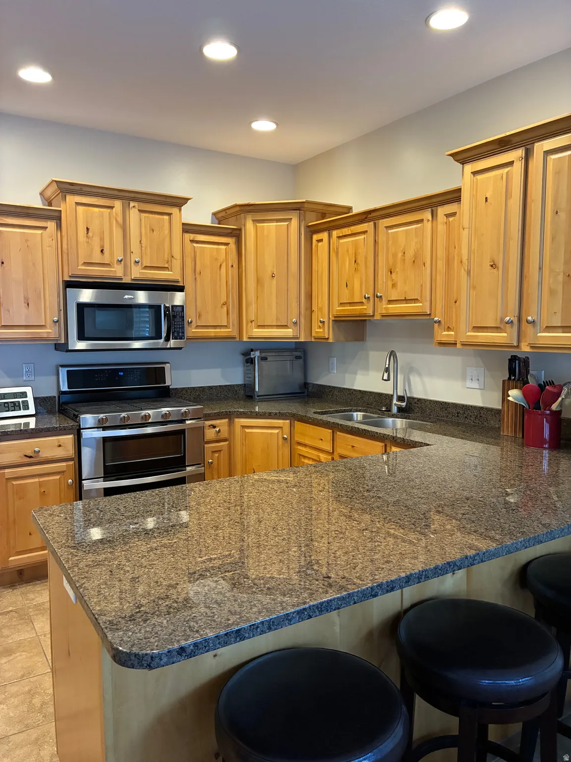 Recessed lighting illuminating the kitchen with wood cabinetry, stainless steel appliances, and stone countertops