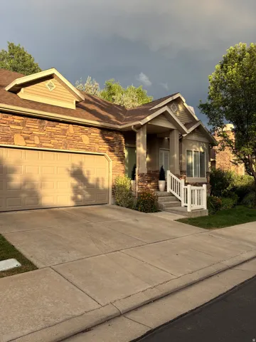 Stone facade accents, an integrated garage, a covered entry, exterior stairs with white railings, and a concrete driveway