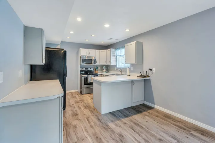 Kitchen featuring wood-finish flooring, white cabinetry, light countertops, stainless steel appliances, and recessed lighting